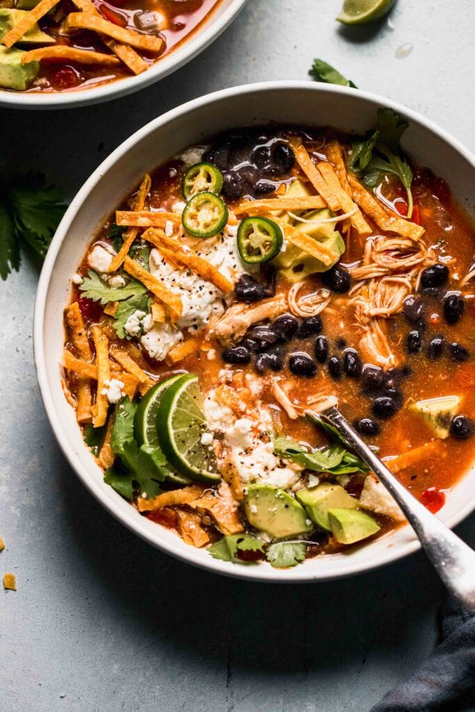 Overhead close up of bowl of slow cooker chicken tortilla soup in bowl with toppings.