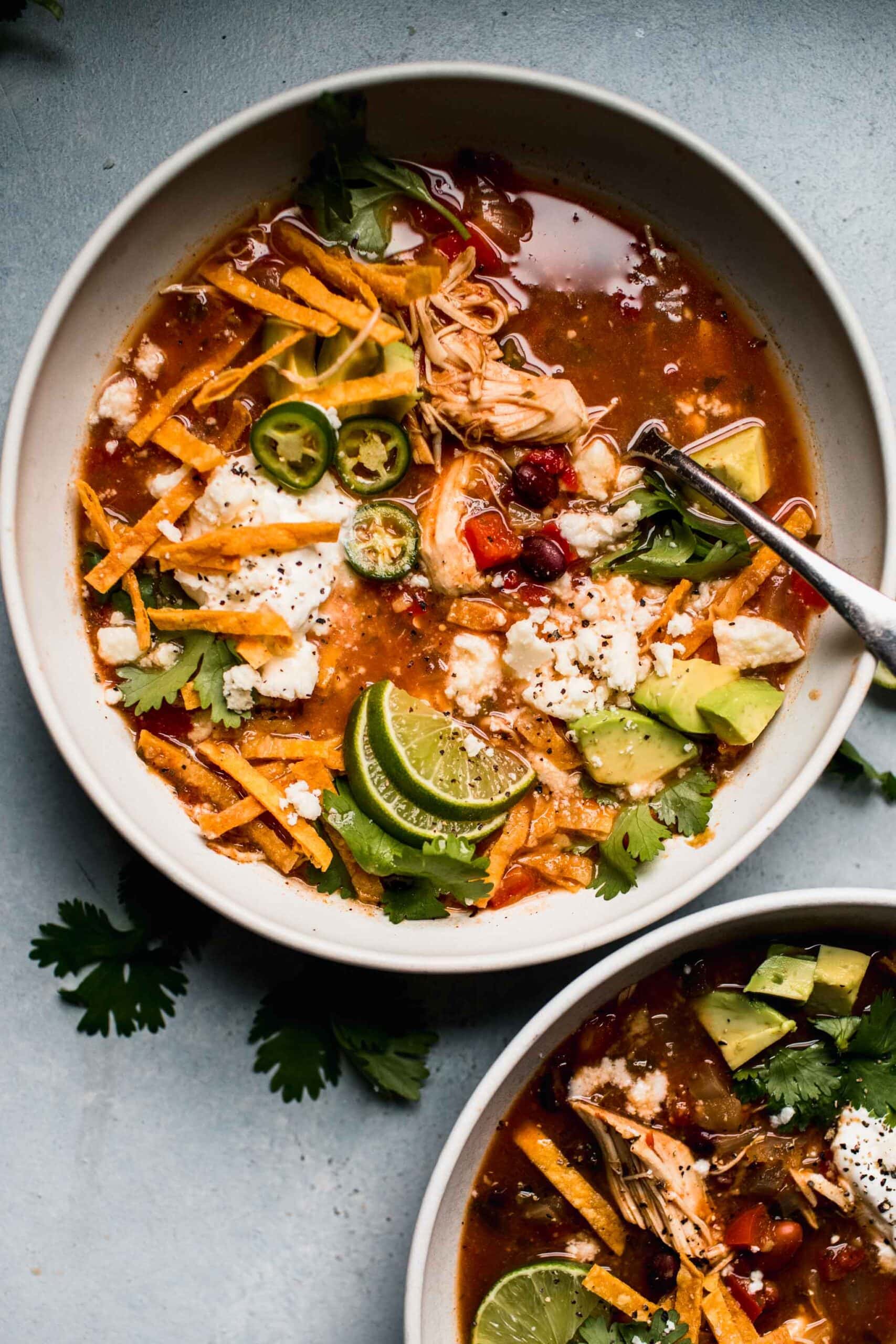 Two bowls of tortilla soup with toppings. 