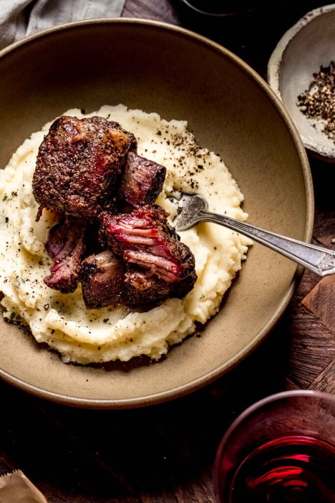 Smoked short ribs in brown bowl on top of mashed potatoes.