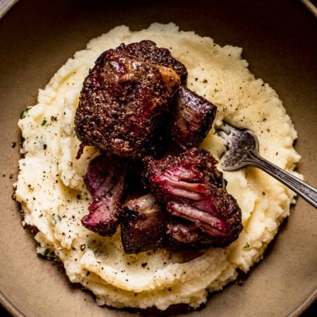 Two smoked beef short ribs in brown bowl on top of mashed potatoes.