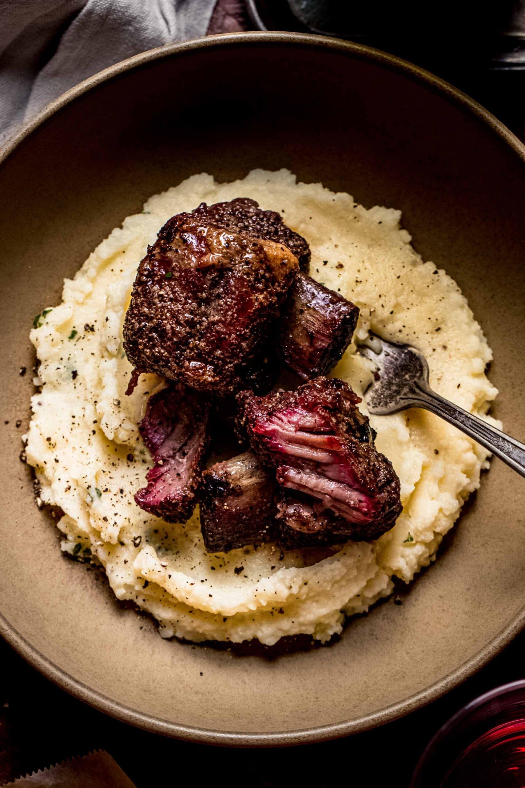 Two smoked beef short ribs in brown bowl on top of mashed potatoes.