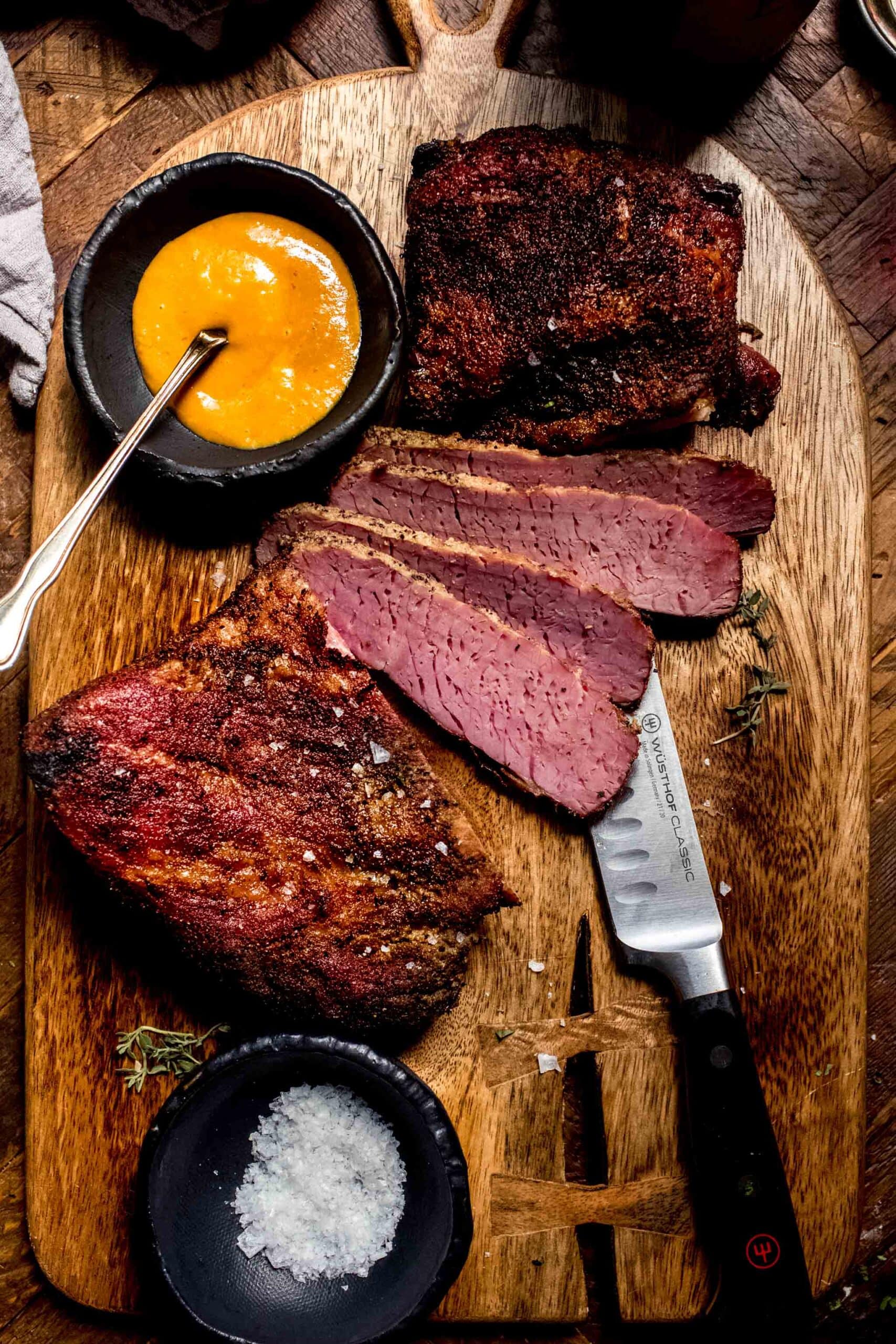 Sliced smoked corned beef on cutting board next to small bowl of honey mustard sauce.