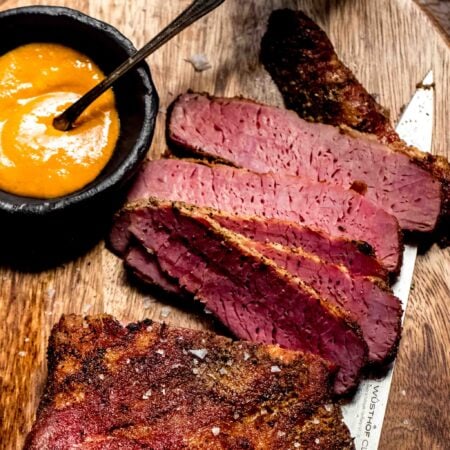 Sliced smoked corned beef on wood cutting board with knife.