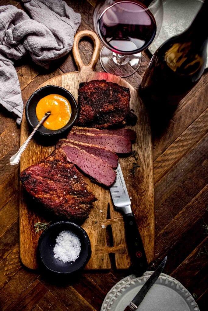 Sliced corned beef ready to be served with plates and bottle and glass of wine on counter. 