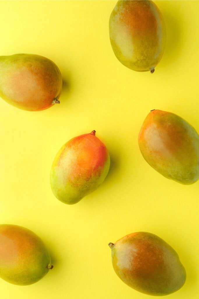 Whole mangoes on bright yellow background. 