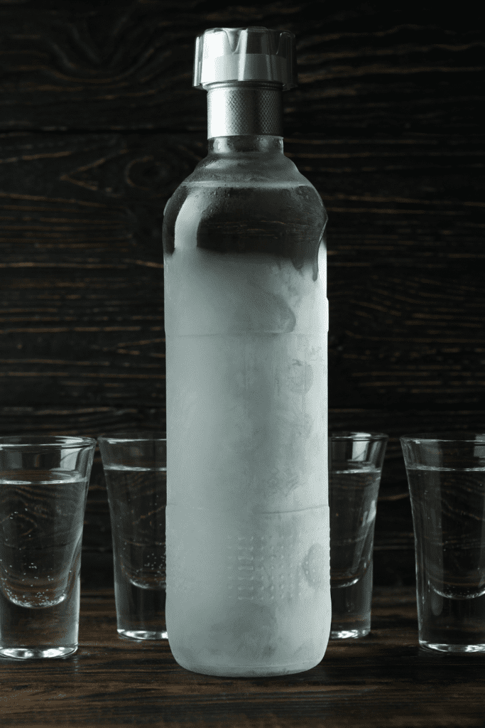 Icy vodka bottle next to shot glasses. 