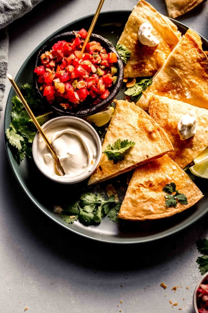 Cooked air fryer quesadillas arranged on plate with toppings. 