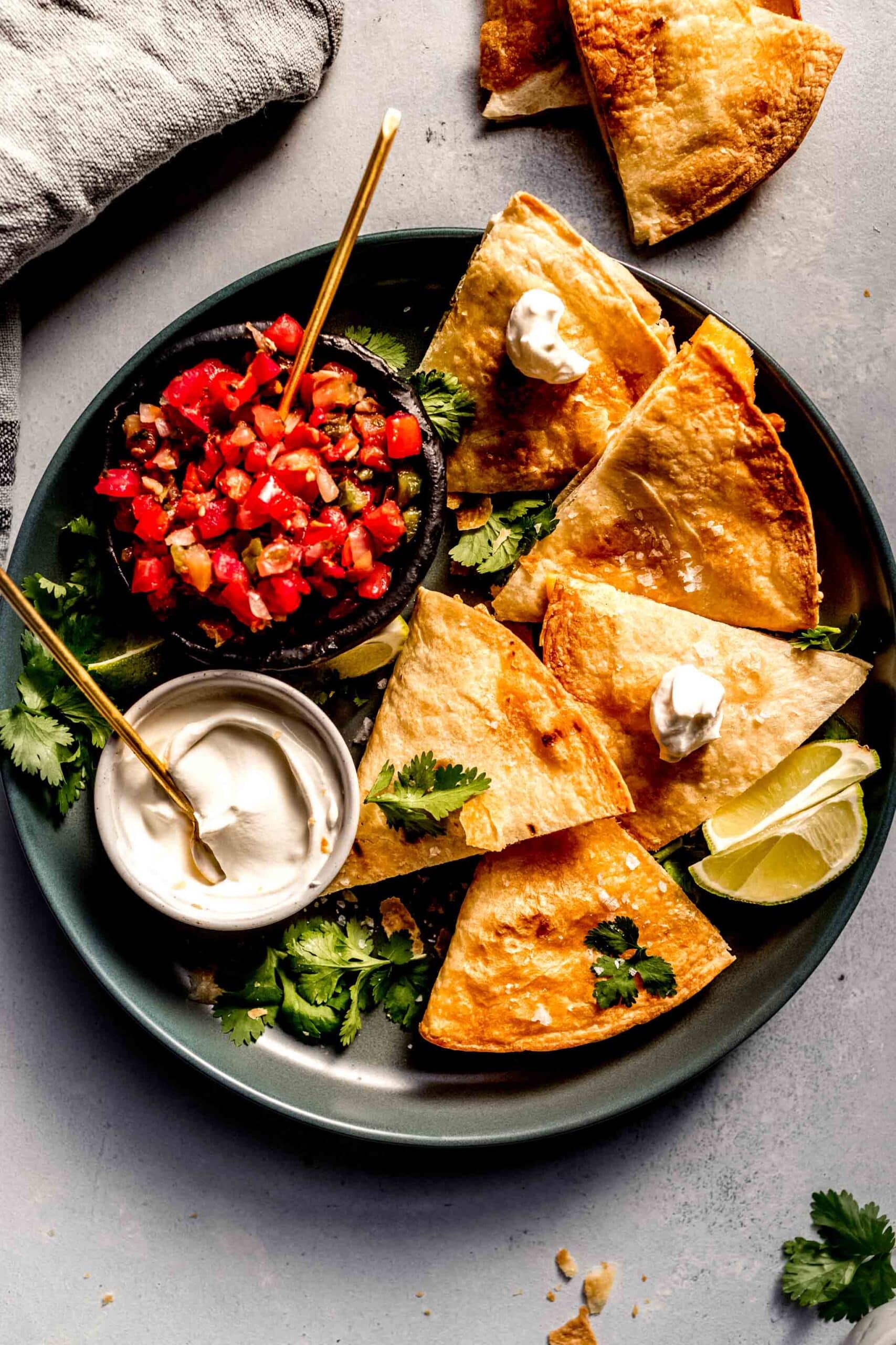 Quesadillas arranged on plate with sour cream and pico de gallo.