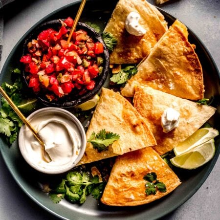 Quesadillas arranged on plate with sour cream and pico de gallo.