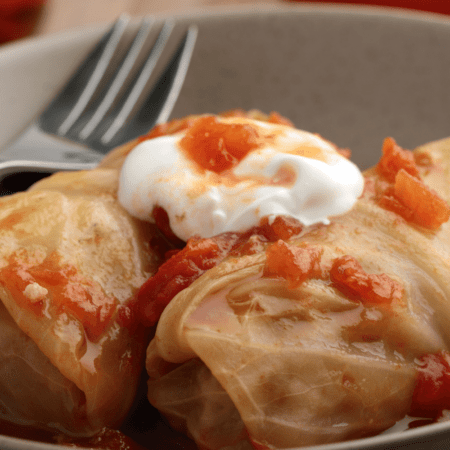 Cabbage rolls in grey bowl topped with sour cream.