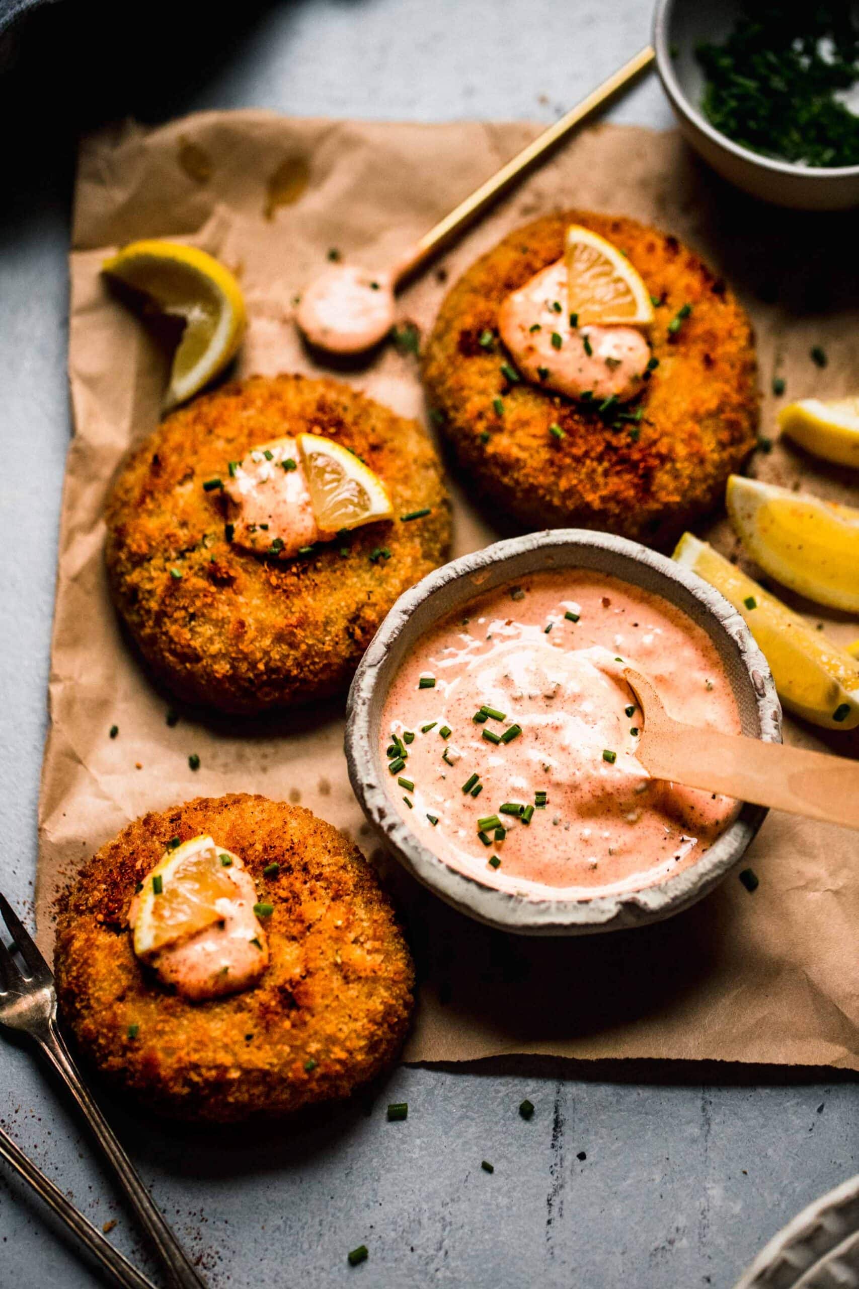 Crab cakes topped with lemon wedges and dollops of crab cake sauce.