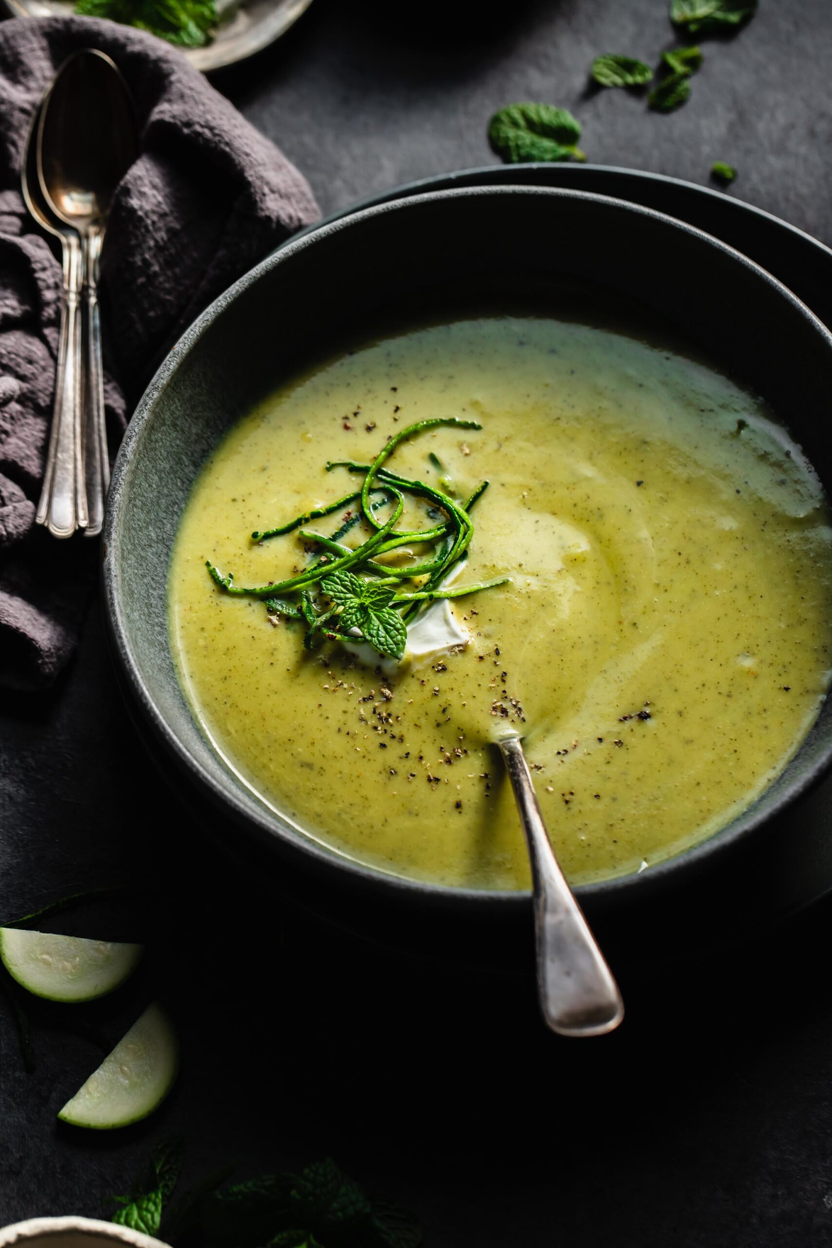 Side view of zucchini soup in grey bowl topped with sour cream and julienned zucchini.