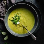 Overhead shot of bowl of creamy zucchini soup in dark grey bowl on dark grey counter.