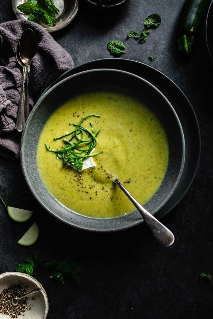 Overhead shot of bowl of creamy zucchini soup in dark grey bowl on dark grey counter.