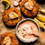 Crab cakes topped with lemon wedges and dollops of crab cake sauce.