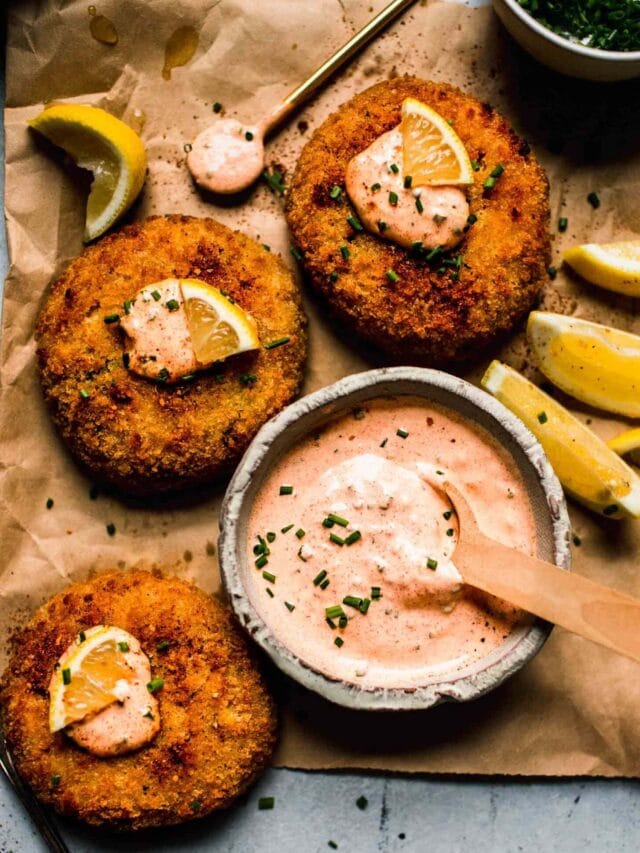 Crab cakes topped with lemon wedges and dollops of crab cake sauce.