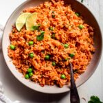 Overhead shot of Mexican rice in white bowl topped with lime wedges.