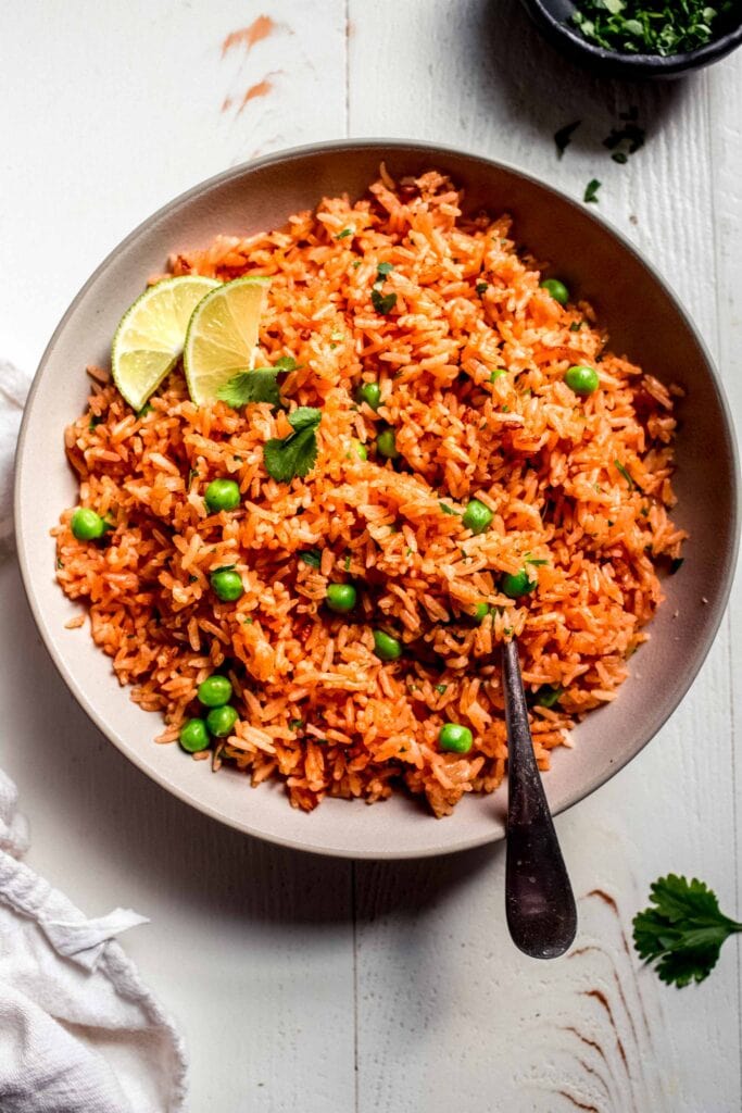 Overhead shot of Mexican rice in white bowl topped with lime wedges.