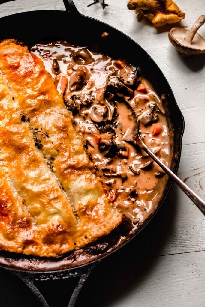 OVERHEAD close up SHOT OF MUSHROOM POT PIE IN SKILLET WITH SCOOP OUT OF IT.