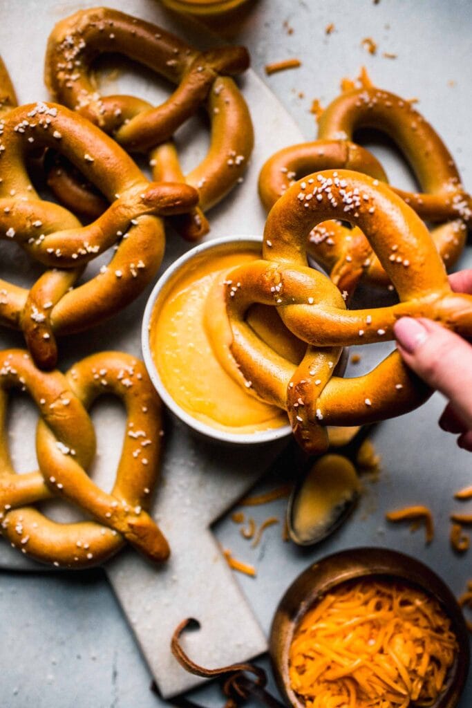 Hand dipping pretzel into cheese sauce. 