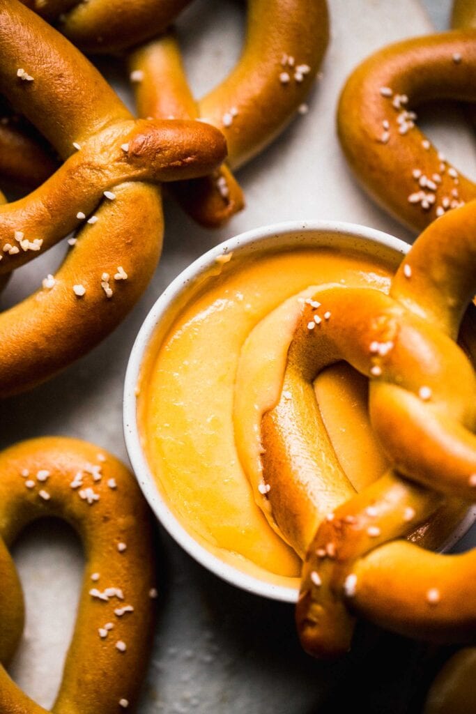 Overhead close up of pretzel dipped in cheese sauce.