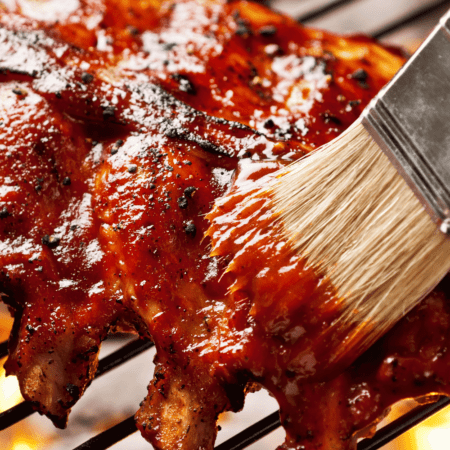 Ribs being brushed with sauce on grill.