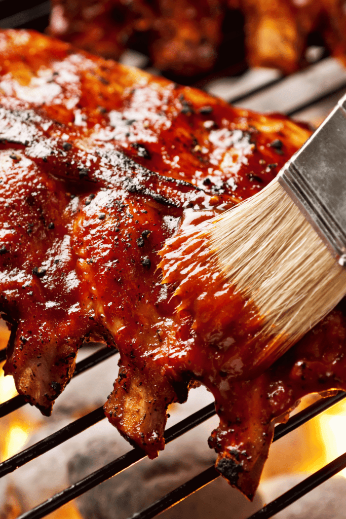 Ribs being brushed with sauce on grill. 