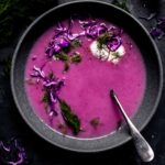 Overhead shot of red cabbage soup in grey bowl topped with sour cream and dill.