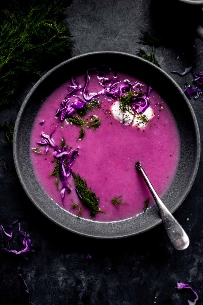 Overhead shot of red cabbage soup in grey bowl topped with sour cream and dill.