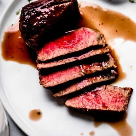 Sliced steak on plate drizzled with red wine sauce.