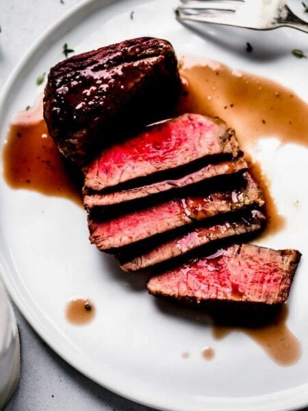 Sliced steak on plate drizzled with red wine sauce.
