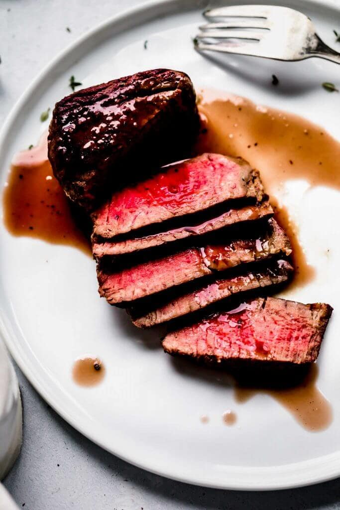 Sliced steak on plate drizzled with red wine sauce.