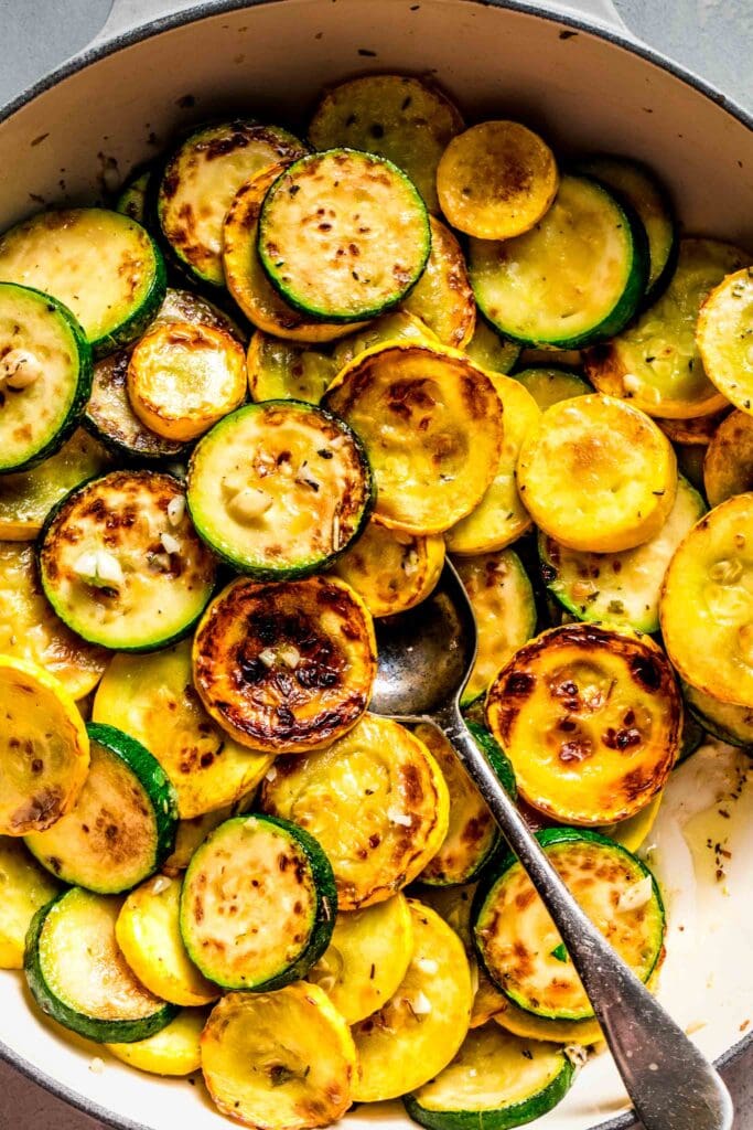 Cooked sliced zucchini and squash in skillet with serving spoon. 