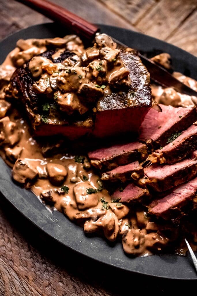 Side view of sous vide roast beef sliced and drizzled with creamy mushroom sauce.