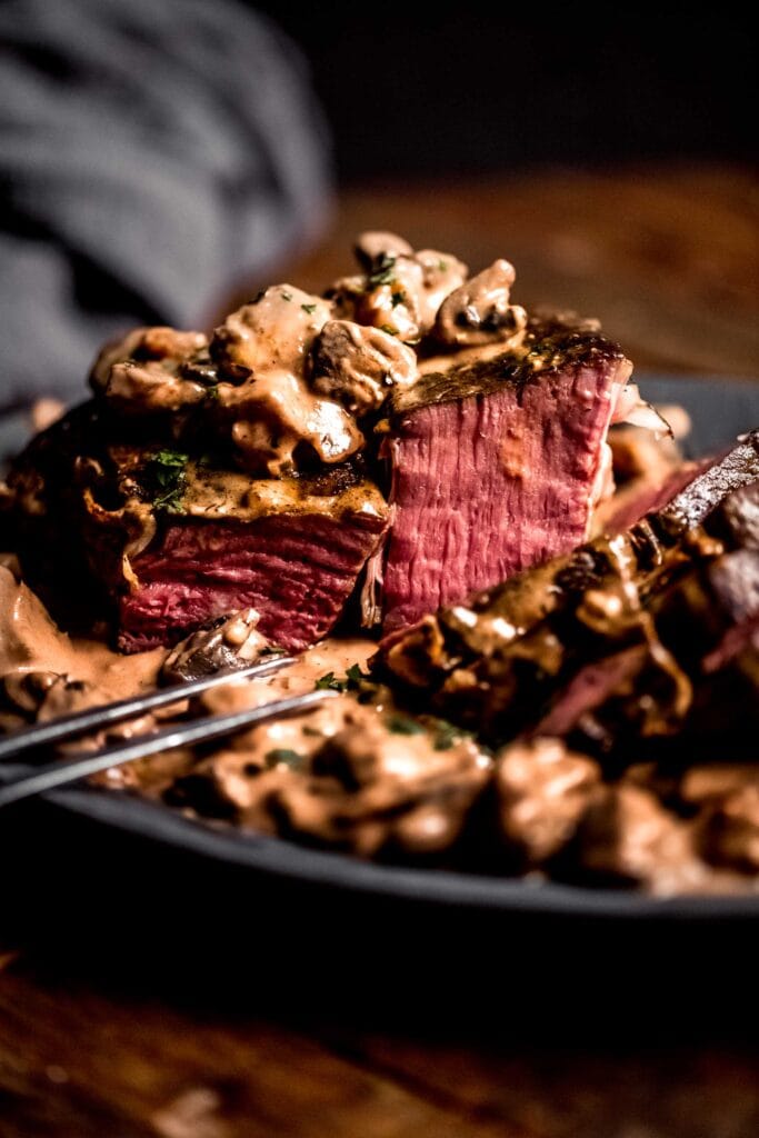 Side view of sous vide roast beef sliced and drizzled with creamy mushroom sauce.