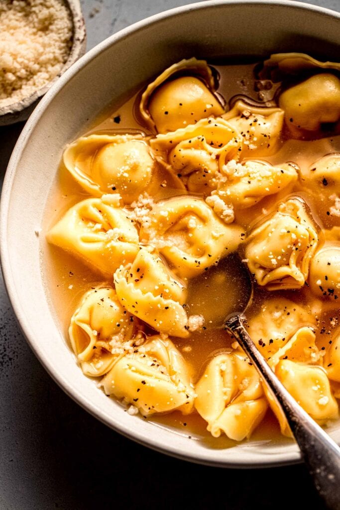 Side view of tortellini in broth sprinkled with parmesan. 