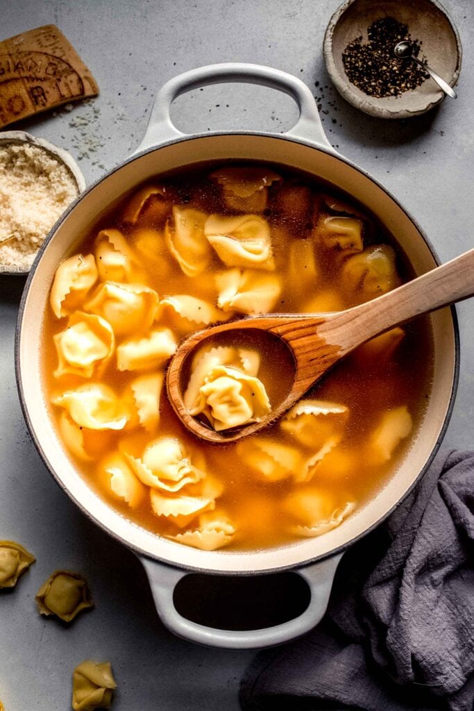 Tortellini soup in pot with ladle. 