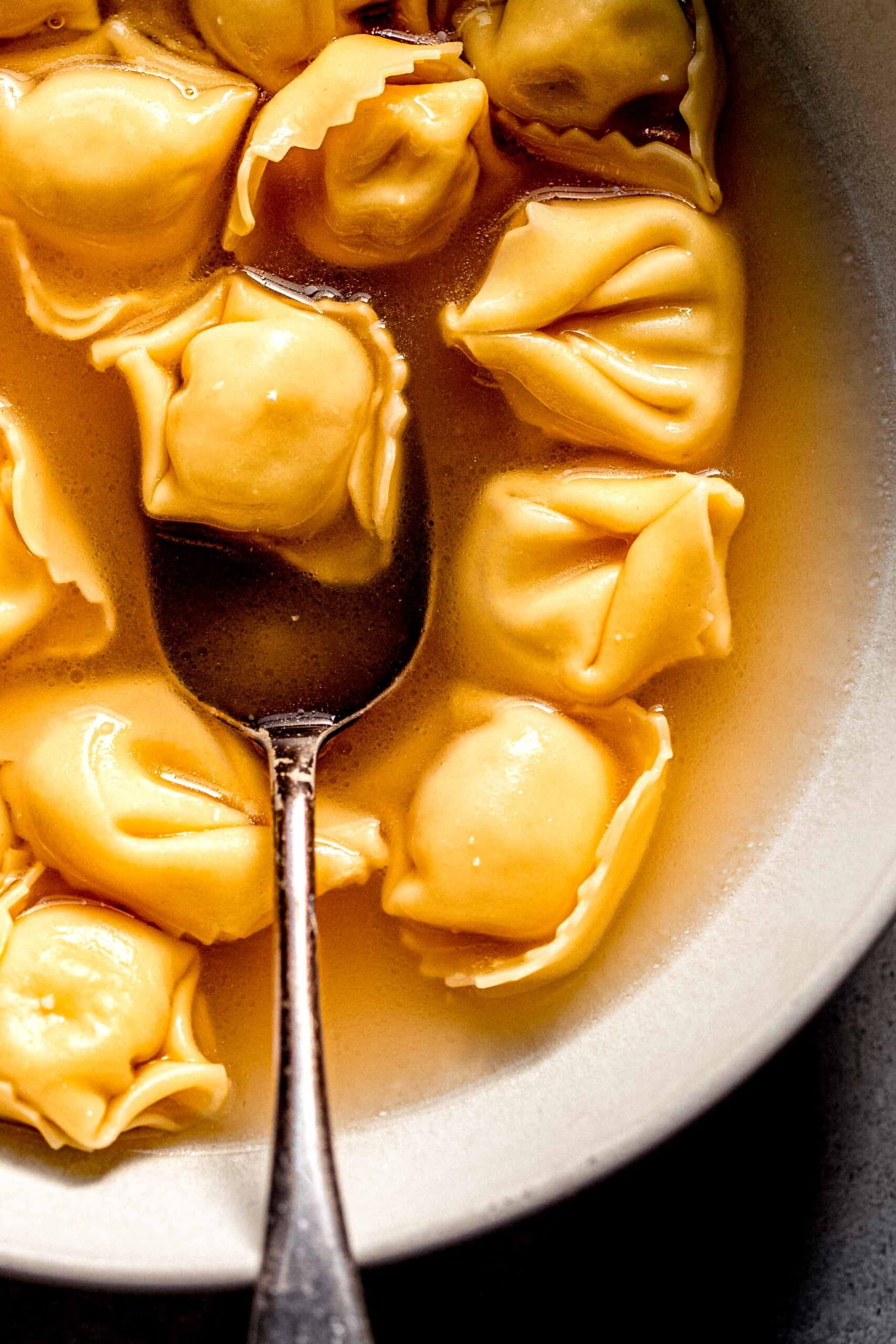 Piece of tortellini on spoon in bowl of broth.