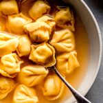 Bowl of tortellini in broth with spoon.