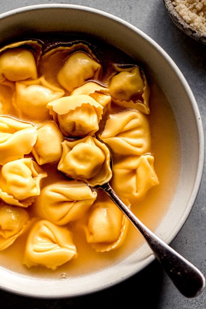 Bowl of tortellini in broth with spoon.