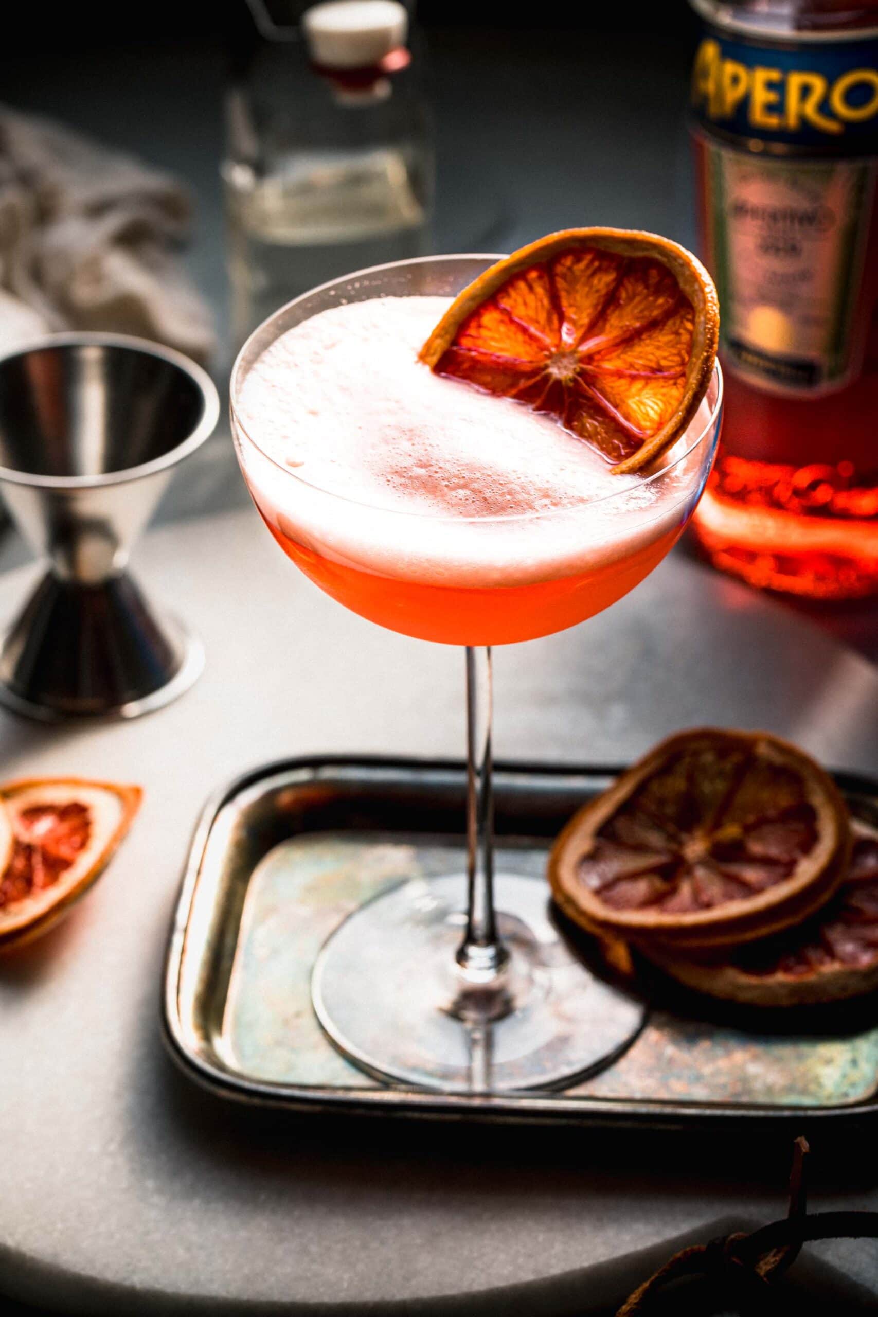 APEROL FIZZ ON SMALL SERVING TRAY GARNISHED WITH DRIED ORANGE WHEEL.