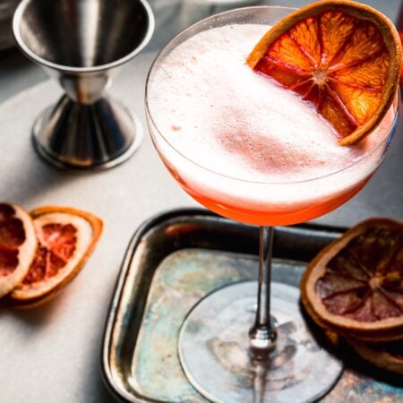 APEROL FIZZ ON SMALL SILVER TRAY NEXT TO JIGGER AND ORANGE SLICES.