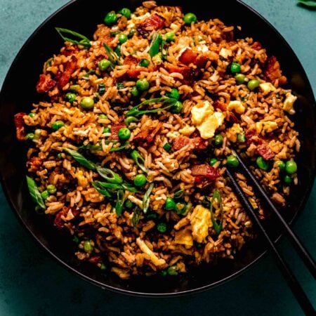 Overhead shot of bacon fried rice in black bowl on teal counter.