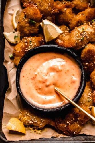 Bang bang sauce in small black bowl with serving spoon.