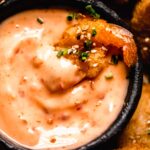 Close up of shrimp dipped into small bowl of bang bang sauce.
