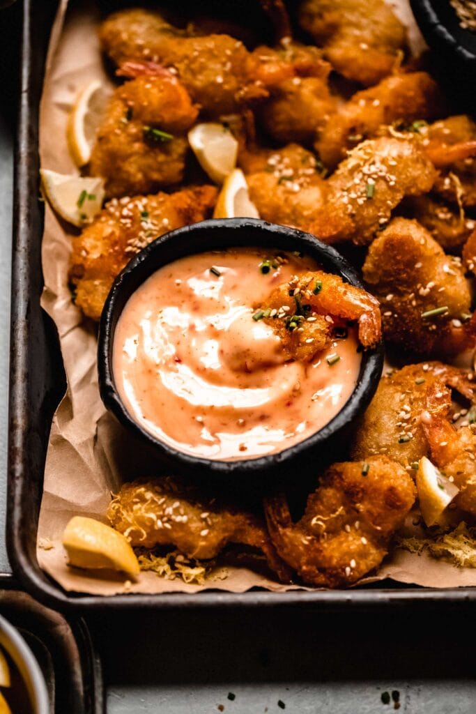 Bang bang sauce on tray surrounded by breaded shrimp.