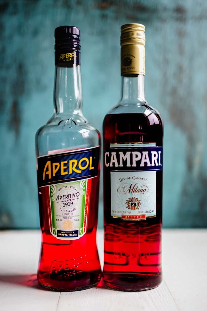 Bottles of aperol and campari against blue background.