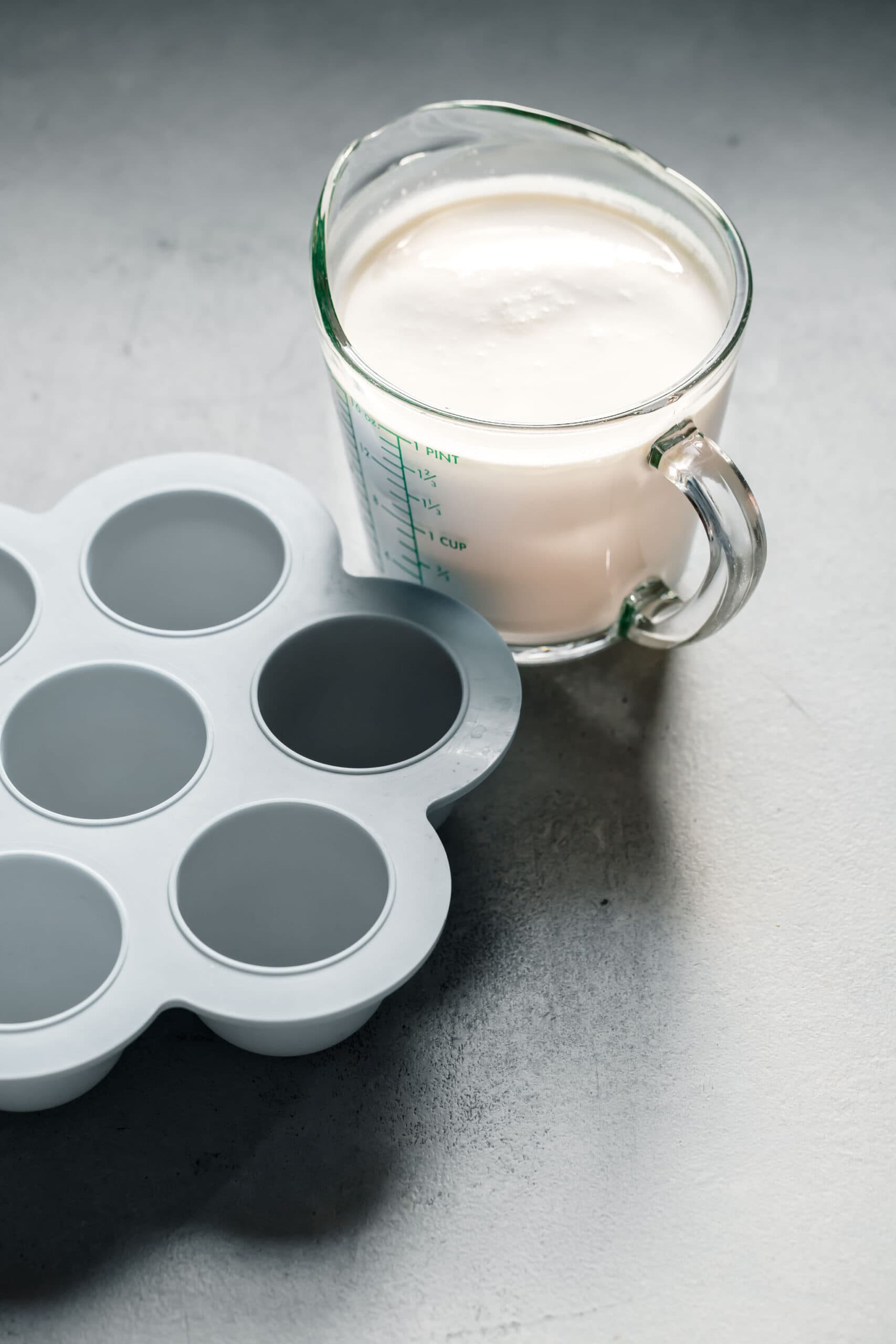 Measuring cup of cream next to silicone mold. 