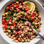 Tuna chickpea salad in bowl with lemon wedges and serving spoon.