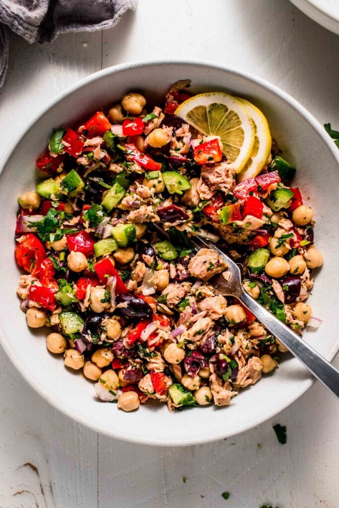 Tuna chickpea salad in bowl with lemon wedges and serving spoon.